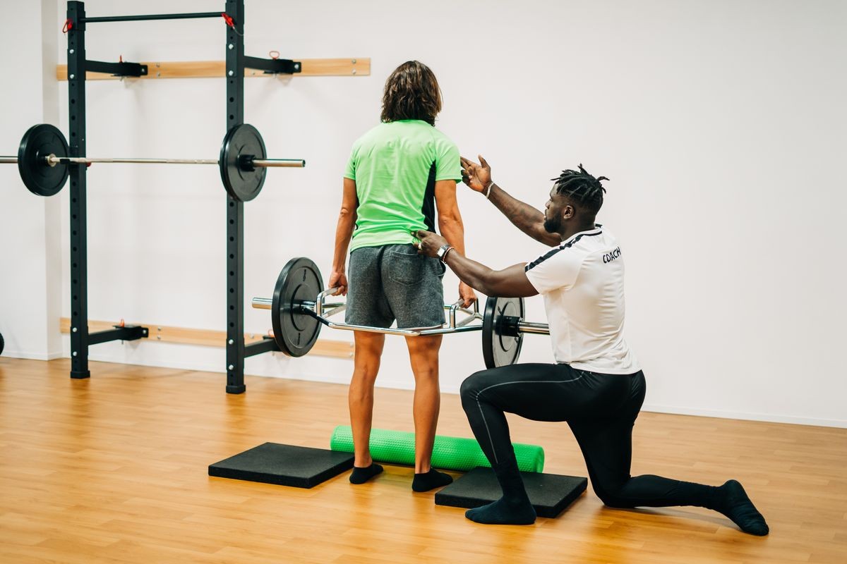 Black man coach training barbell with his patient in gym